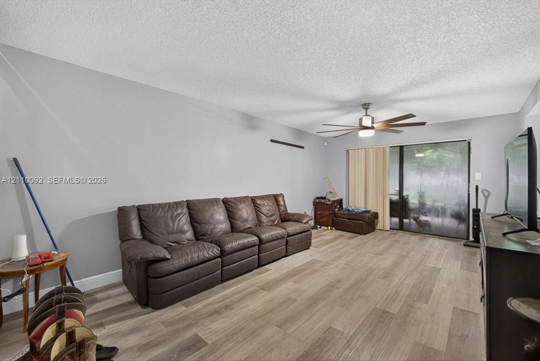 Living space featuring wood-finish flooring, a multi-blade ceiling fan with integrated lighting, and a sliding glass door providing external access
