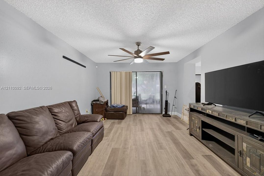 Wood-finish flooring, multi-blade ceiling fan with integrated lighting, and glass sliding door