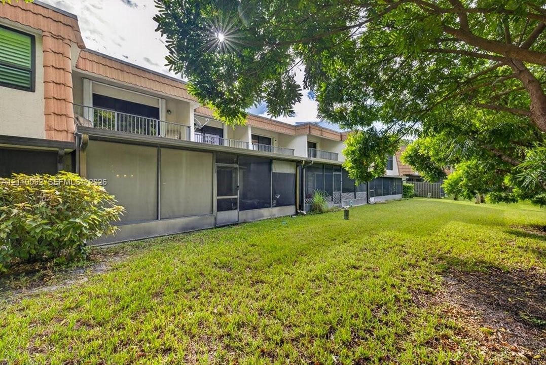 Backyard featuring a grass lawn, screened-in ground-level patio, upper-level balconies with metal railings, and tile roof detailing