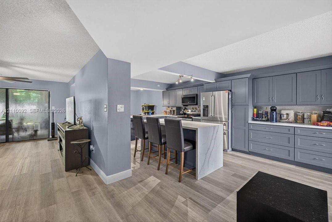 Kitchen featuring gray shaker-style cabinetry, white waterfall-edge stone island, stainless steel appliances, and wood-finish flooring
