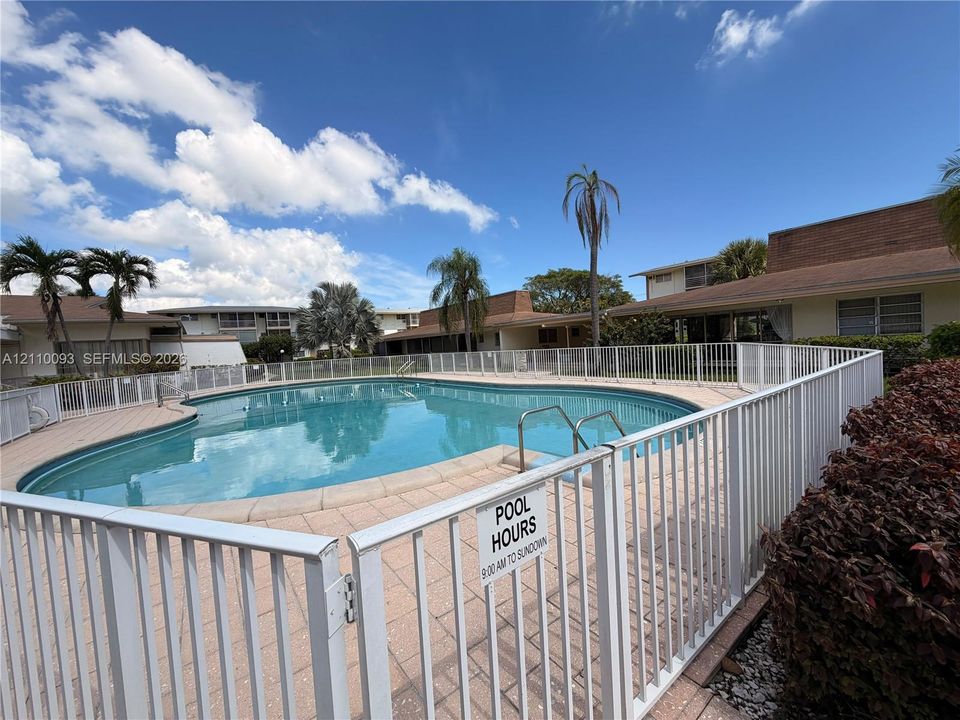 In-ground swimming pool featuring a concrete surround, metal perimeter fencing, and stainless steel pool ladder
