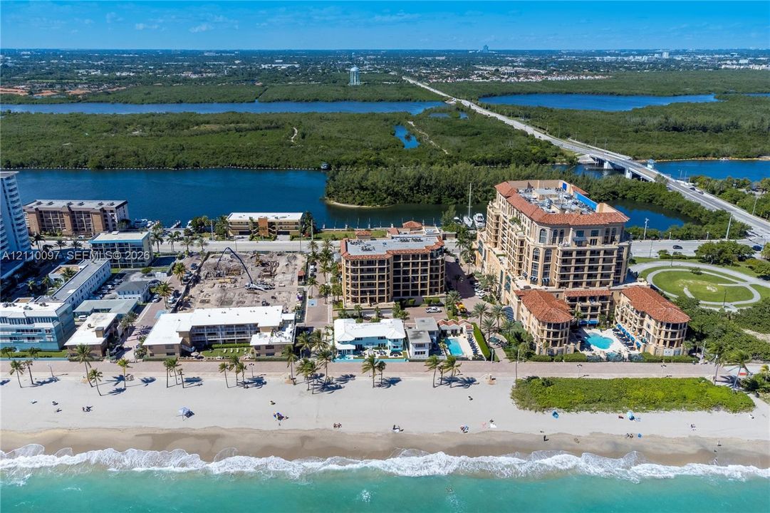 Aerial perspective of beachfront property featuring direct ocean access, building-integrated swimming pools, terracotta-style roofing, and multi-level balconies