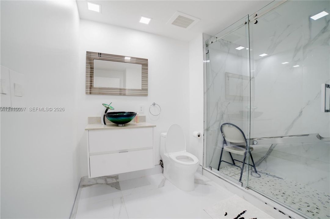 Bathroom featuring a floating vanity with a vessel sink, walk-in shower with stone-pattern wall tile, recessed lighting, and large-format flooring