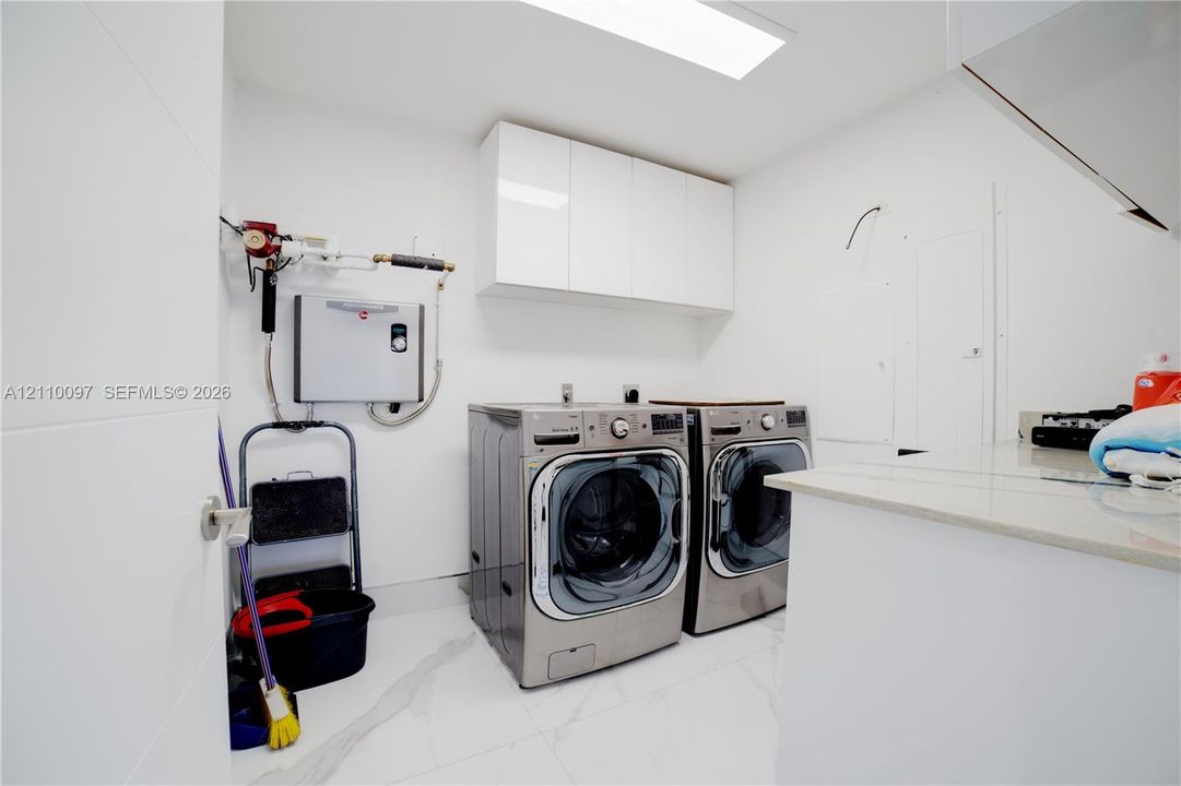 Laundry room featuring white high-gloss cabinetry, stone-finish countertops, and large-format tile flooring