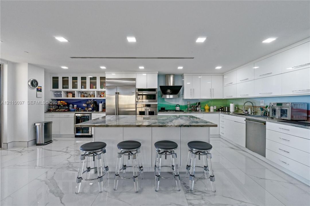Modern kitchen featuring high-gloss cabinetry, a central island with natural stone countertop, stainless steel appliances, and large-format tile flooring