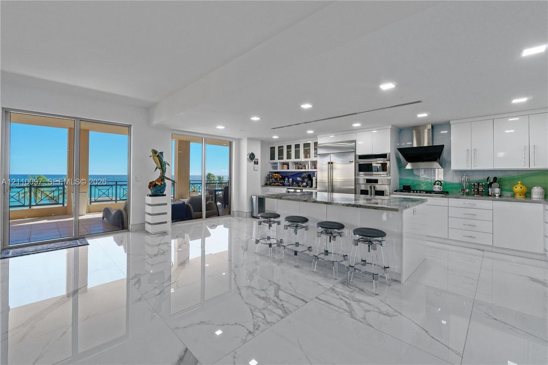 Kitchen featuring glossy cabinetry, a central island with stone countertop, stainless steel appliances, large-format tile flooring, and floor-to-ceiling glass sliding doors