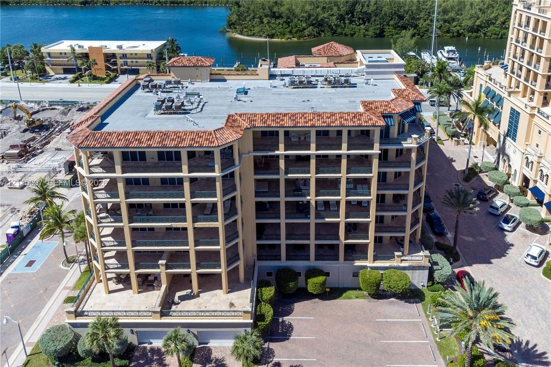 Multi-story building with a terracotta tile roof, structural balconies, paved surface parking, and exterior palm landscaping