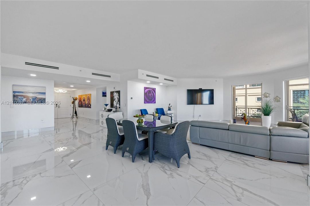 Open-concept interior featuring large-format polished stone-finish flooring, recessed lighting, integrated ceiling linear air registers, and floor-to-ceiling glass door access to a balcony