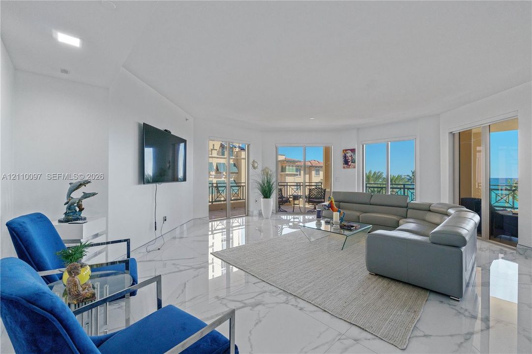 Sophisticated high-rise living room showcasing floor-to-ceiling windows with panoramic cityscape vistas, polished light-toned flooring throughout, and a wall-mounted entertainment system