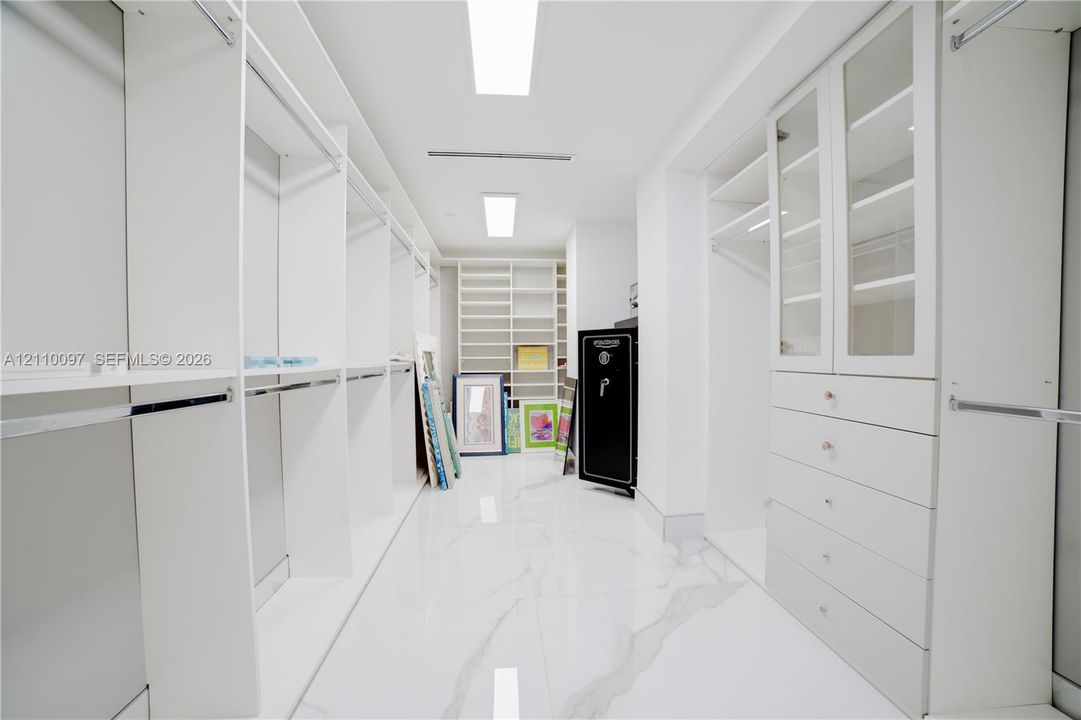 Walk-in closet featuring extensive built-in white cabinetry, glass-fronted upper doors, multiple storage drawers, and polished stone-finish flooring