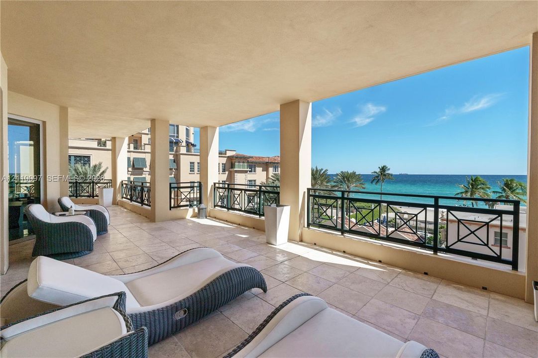 Covered balcony featuring stone-tile flooring, structural support columns, and black metal railings, overlooking the ocean