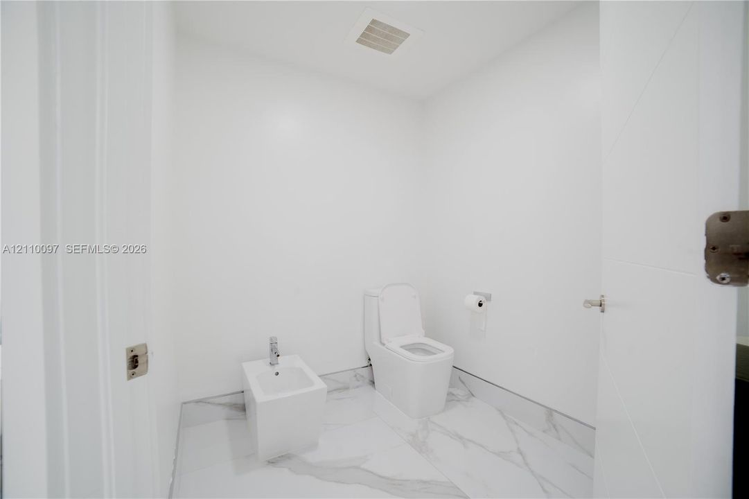 Full-height veined tile flooring, wall-mounted toilet, and bidet with chrome fixtures