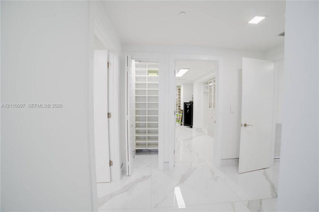 Large-format stone-finish flooring with white and grey veining throughout, featuring multiple walk-in storage areas with custom built-in shelving, white slab-style doors, and recessed lighting