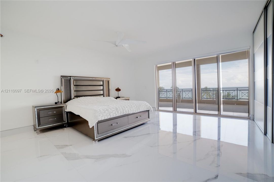 Polished stone flooring, floor-to-ceiling sliding glass doors, built-in closet with sliding panels, ceiling-mounted fan, and private covered balcony