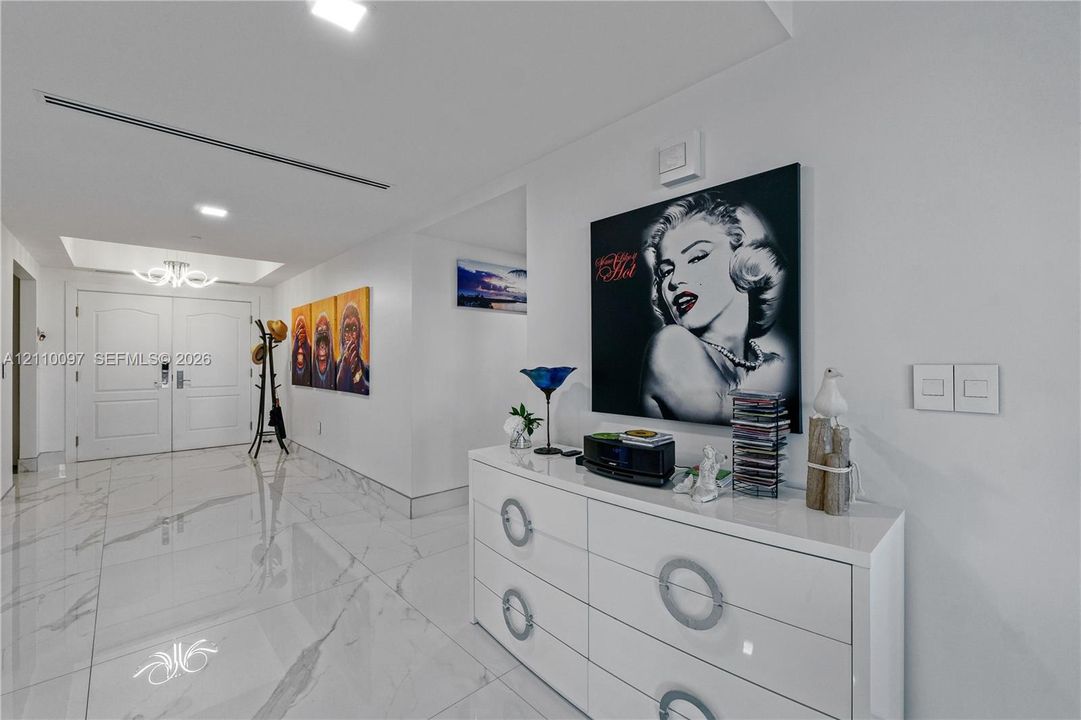 Foyer featuring high-gloss large-format tile flooring, double-door entry with arched panel detailing, recessed ceiling lighting, and a modern tiered chandelier