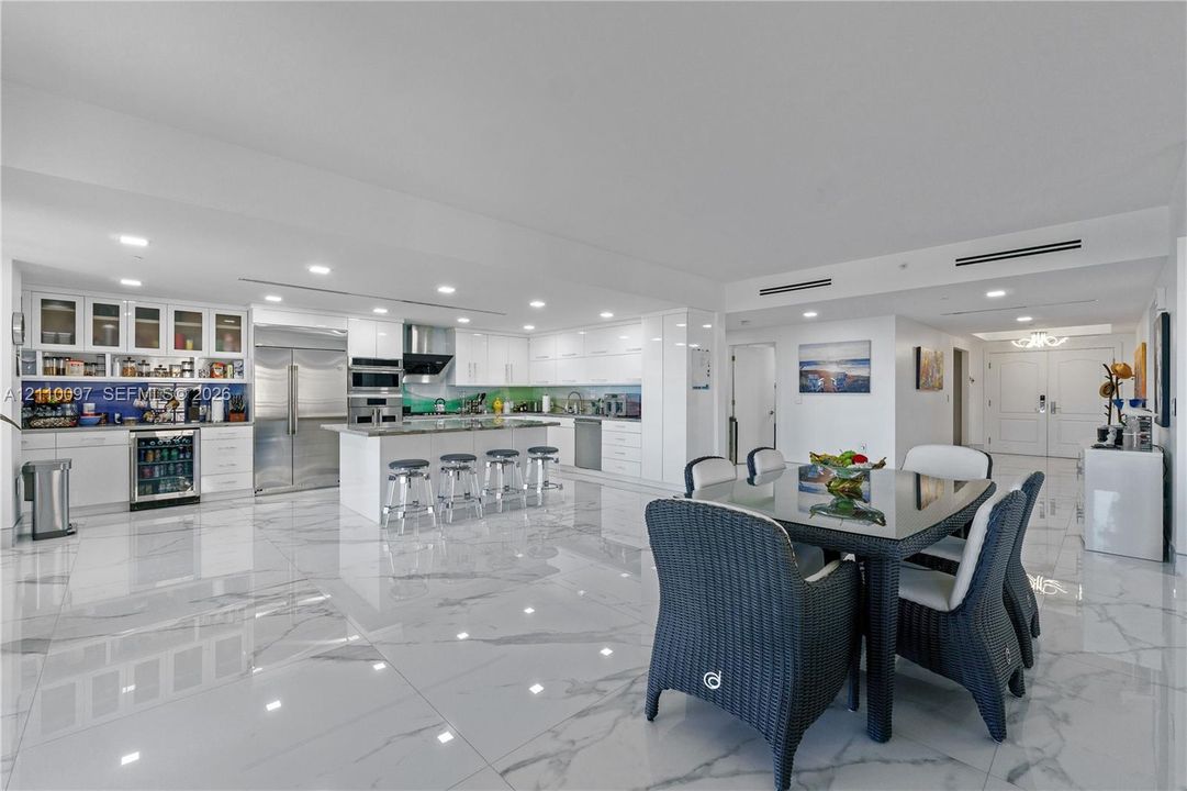 Kitchen featuring white cabinetry, an expansive center island, integrated stainless steel appliances, a beverage refrigerator, and polished stone-finish flooring