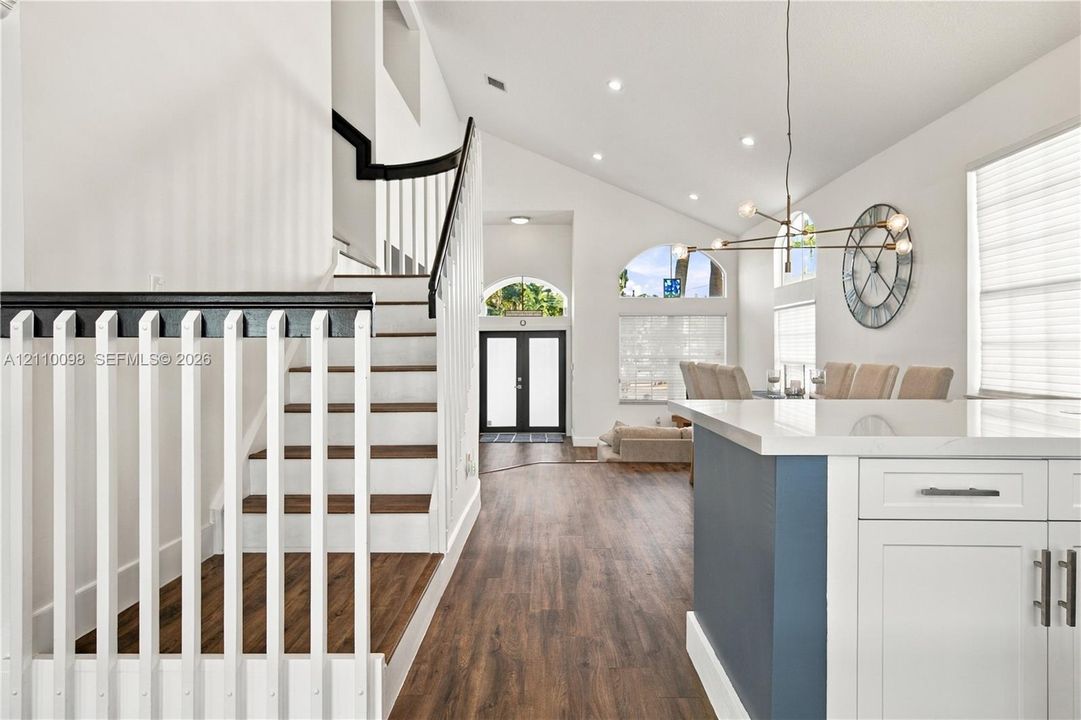 Vaulted ceilings, wood-finish flooring, staircase with contrasting handrail and balusters, architectural arched windows, and kitchen island with white cabinetry