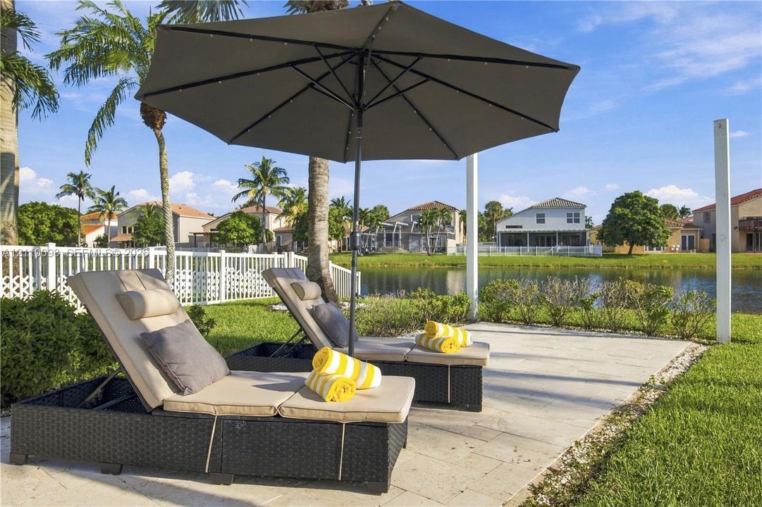 Stone paver patio featuring a white vinyl perimeter fence, mature palm trees, and waterfront grounds