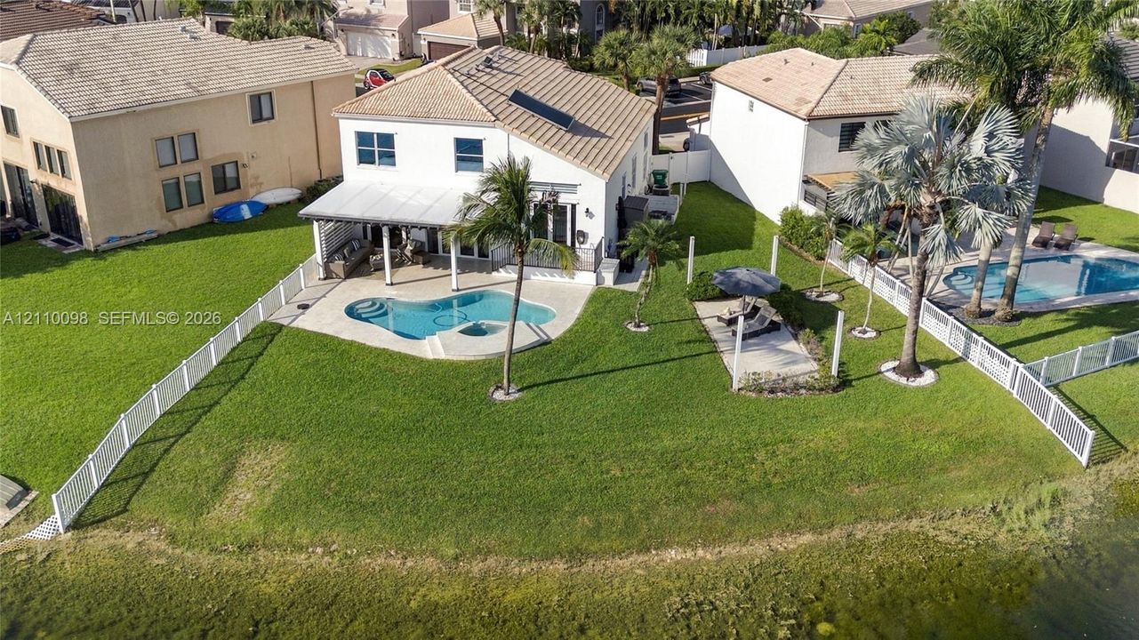 Backyard featuring an in-ground swimming pool, covered patio, white vinyl fencing, mature palm trees, and waterfront access