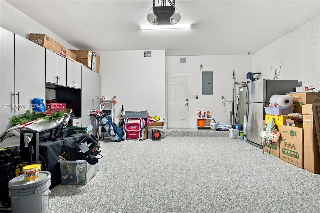Garage featuring an epoxy floor finish, built-in white cabinetry with bar pulls, and a dedicated exterior-access door