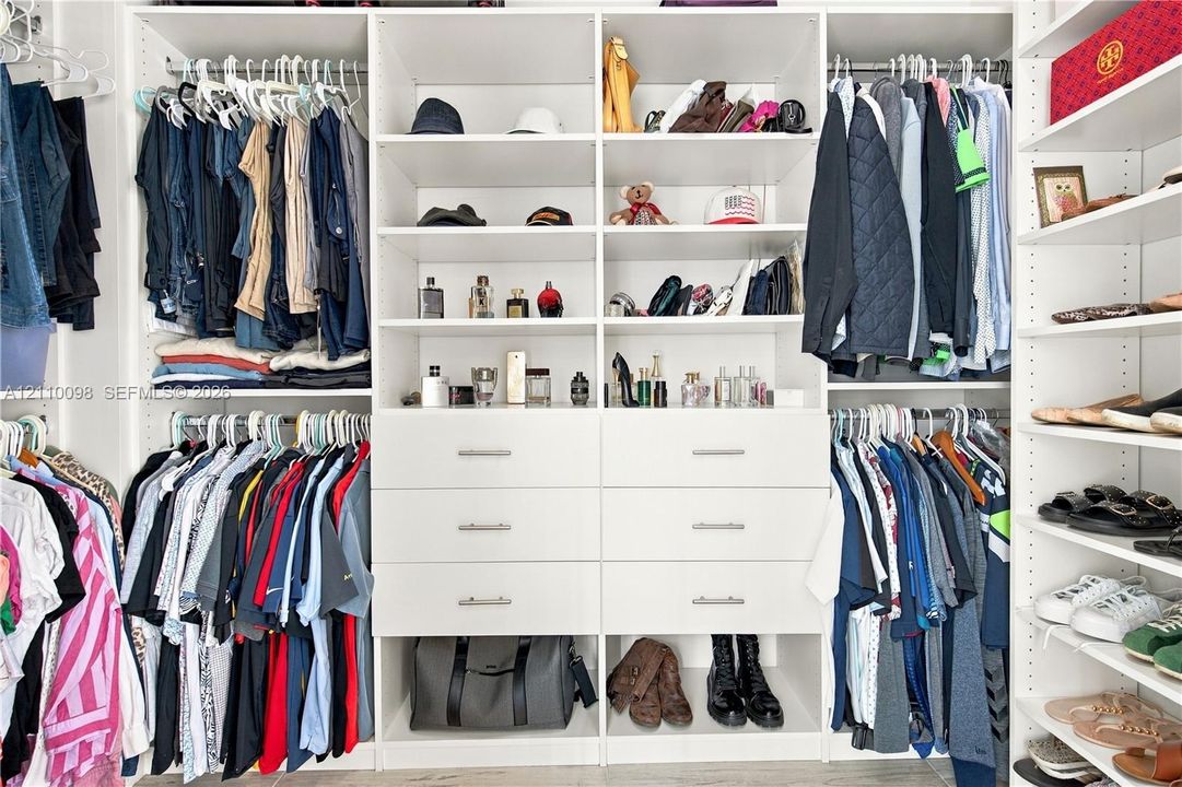 Custom built-in white cabinetry featuring multiple hanging rods, open shelving, and six pull-out drawers with metal pulls