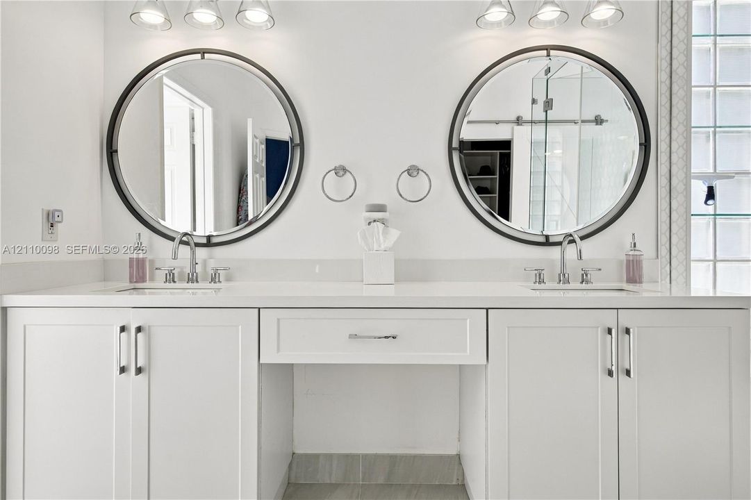 Dual-sink vanity featuring white cabinetry, solid surface countertop, two circular mirrors with dark frames, and chrome fixtures