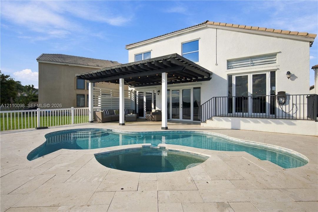 Stucco exterior featuring a covered patio with a wooden pergola, a freeform pool, an attached spa, and stone-paver decking
