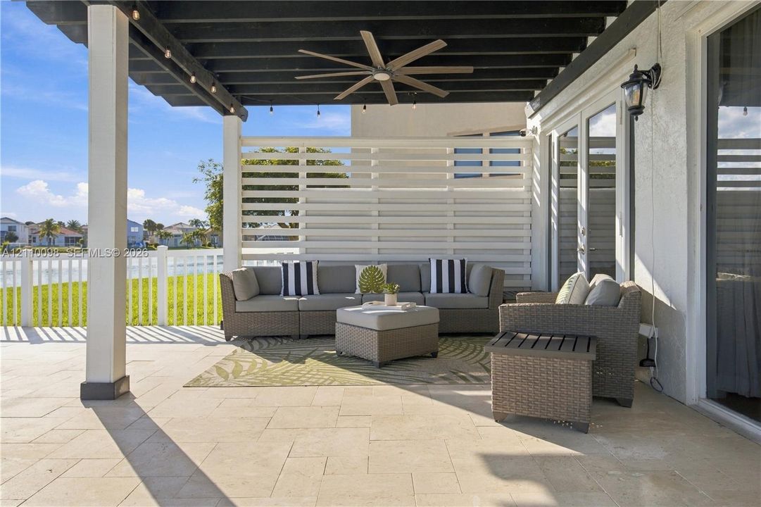 Covered patio featuring stone-tiled flooring, a dark-finished wooden pergola, a ceiling fan, and a white privacy screen