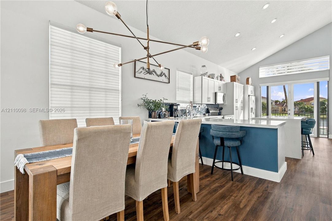 Vaulted ceiling, open-concept kitchen featuring a center island with bar seating, custom white cabinetry, and modern multi-arm chandelier, finished with wood-finish flooring
