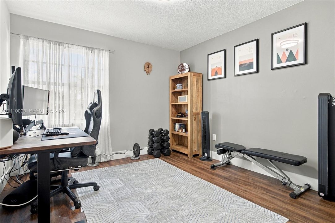 Neutral-toned interior room featuring wood-finish flooring and a single-pane window with adjustable curtains