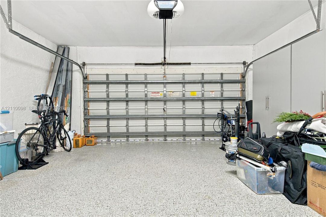 Two-car garage featuring a sectional metal door, epoxy-coated concrete flooring, and ceiling-mounted automatic door opener