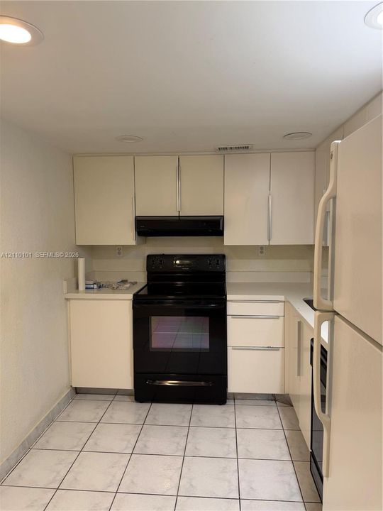 Kitchen featuring matte finish cabinetry, black range, integrated range hood, solid surface countertops, and tile flooring