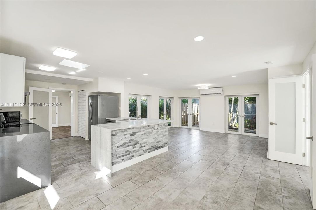 Open-concept kitchen featuring an island with stone-tile cladding and quartz countertops, gray ceramic tile flooring, recessed lighting, and multiple sets of French doors
