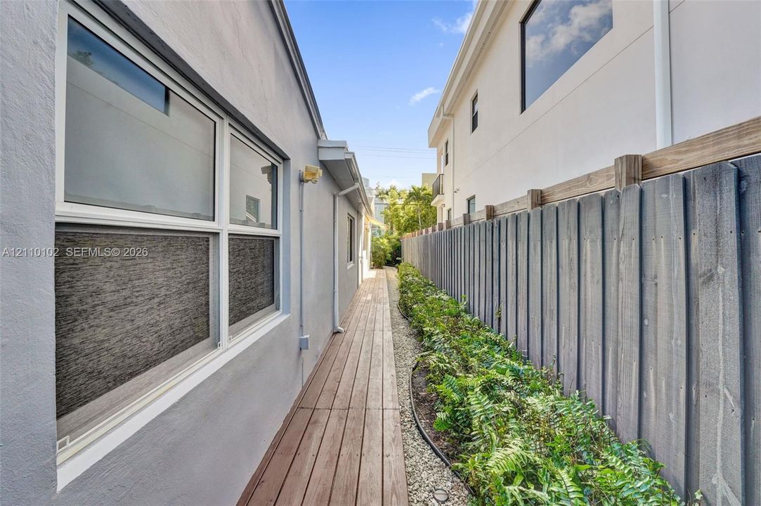 Exterior side walkway featuring wood-plank decking, a vertical wood privacy fence, and integrated landscaping with stone ground cover