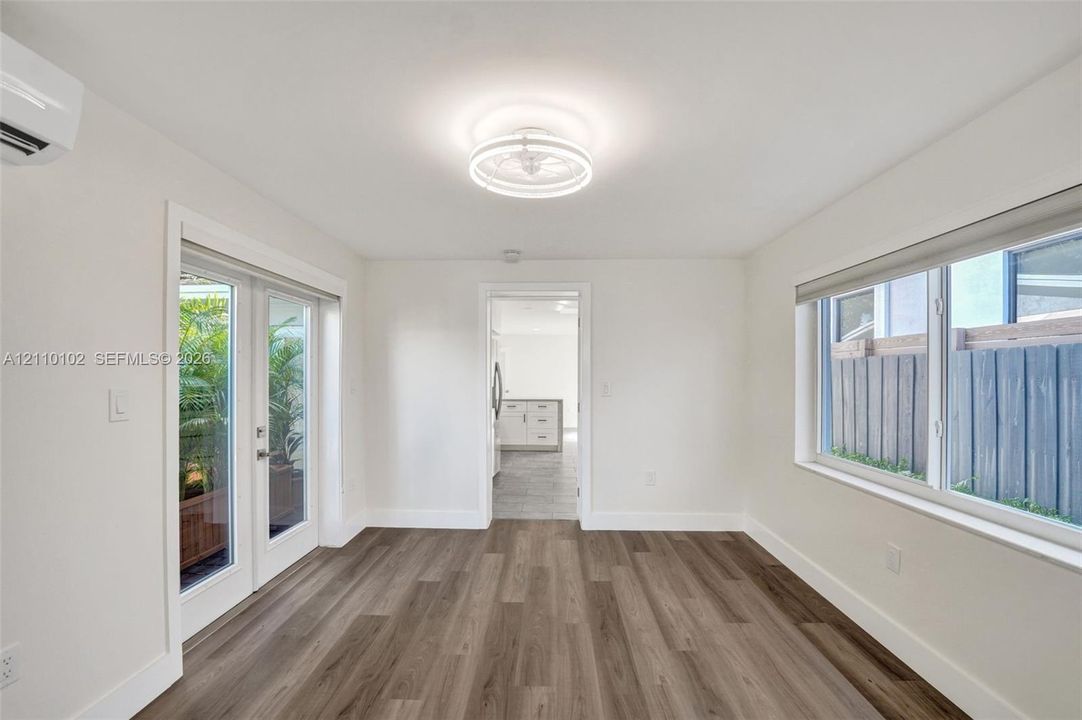 Room featuring wood-finish flooring, a wall-mounted ductless climate control unit, large sliding glass doors, a contemporary circular flush-mount ceiling light fixture, and horizontal windows
