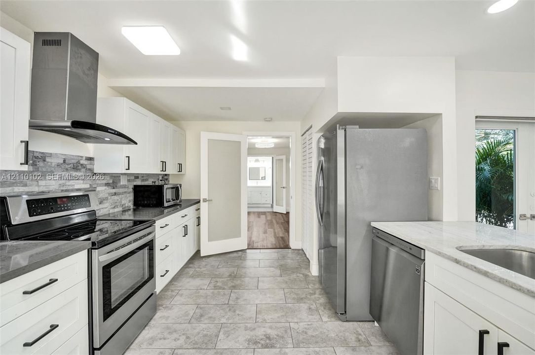 Kitchen featuring white shaker cabinetry, stone-tile backsplash, stainless steel appliances, stone-look countertops, and neutral tile flooring