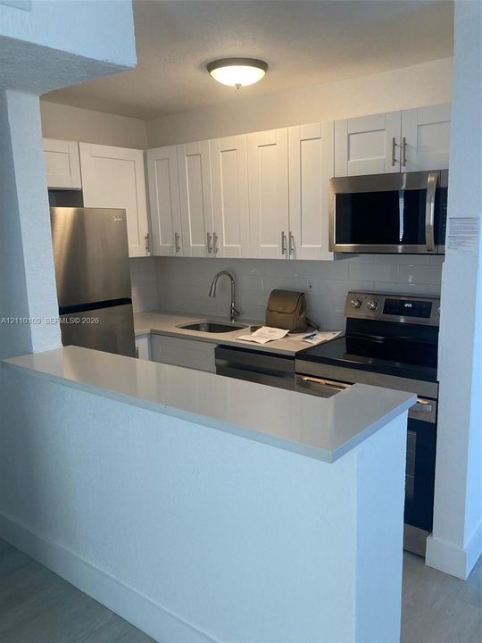 Kitchen featuring white shaker-style cabinetry, quartz countertops, stainless steel appliances, subway tile backsplash, and a breakfast bar