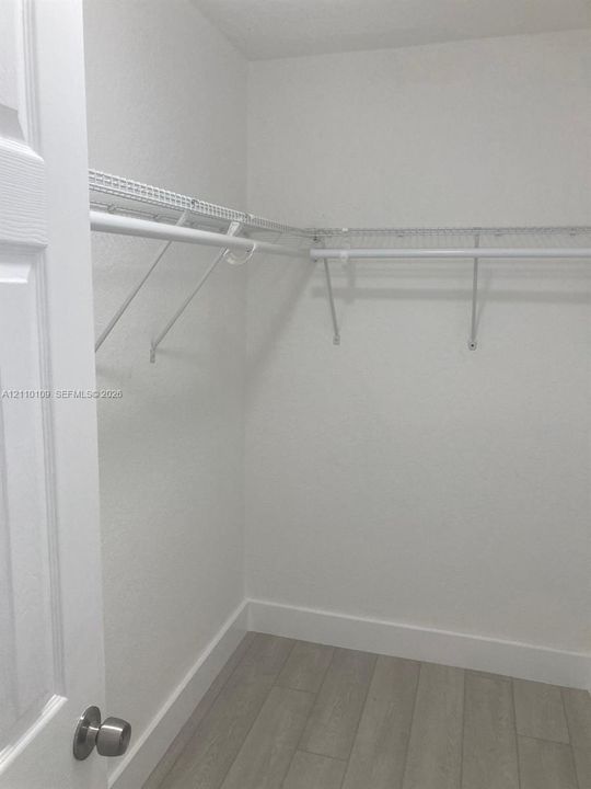 Storage area featuring neutral wood-finish flooring and white wire shelving with integrated hanging rods