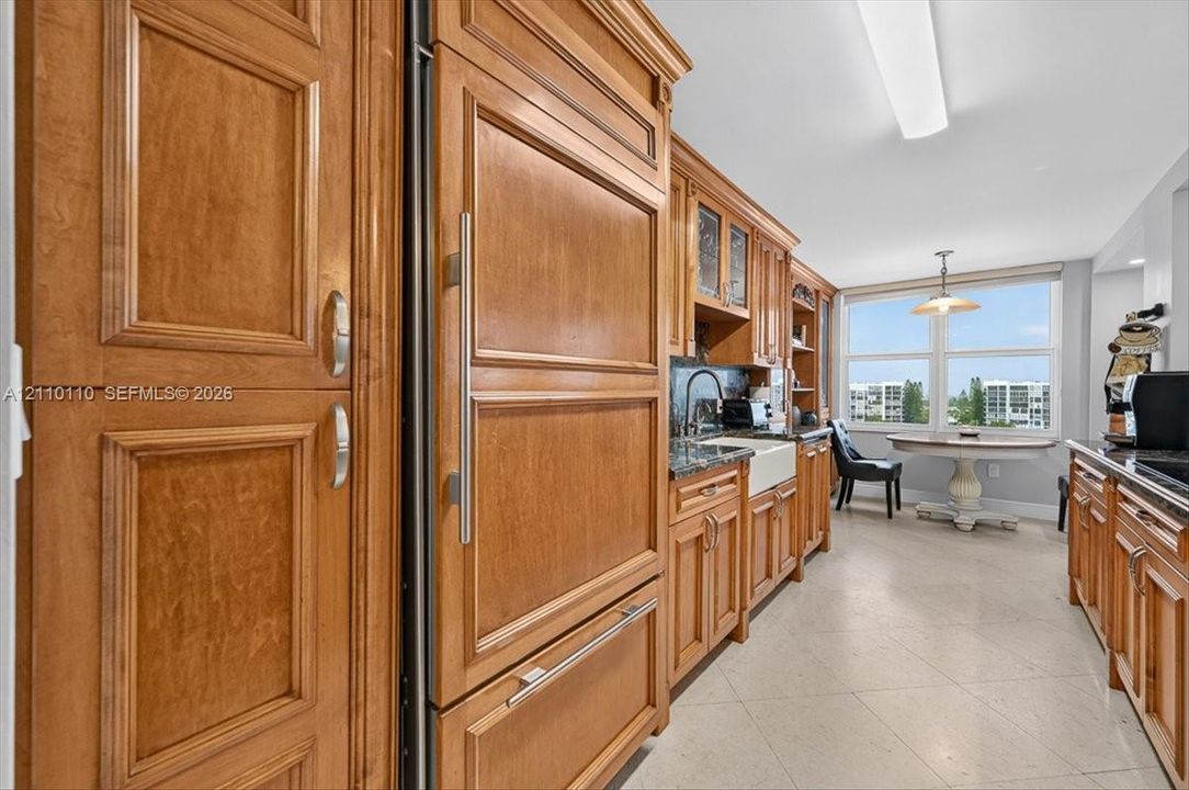 Custom cabinetry with integrated paneled refrigerator, farmhouse sink, dark stone countertops, and tile flooring