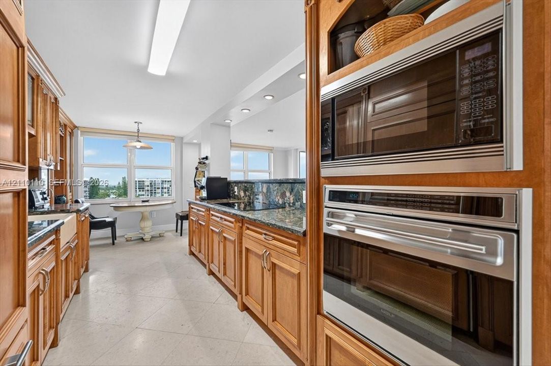 Kitchen featuring wood cabinetry, natural stone countertops, a farm-style apron sink, and built-in stainless steel double wall ovens and microwave