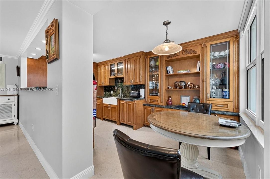 Custom wood cabinetry featuring integrated display shelving and glass-front upper units, apron-front farmhouse sink, stone countertops, and crown molding