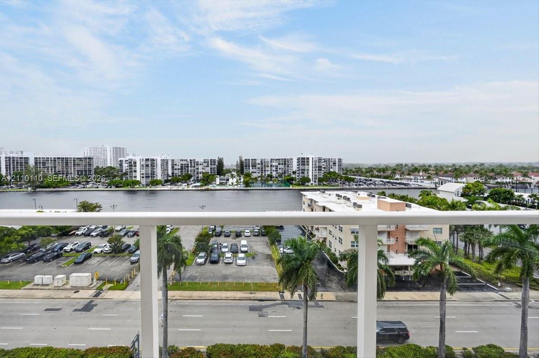 Elevated balcony featuring a white metal railing overlooking a waterway and urban landscape