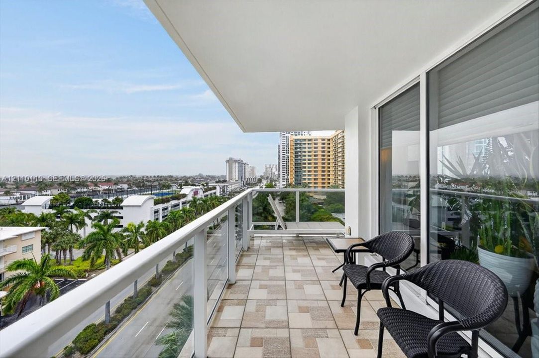 Covered balcony featuring geometric tile flooring, a white metal and glass panel railing, and expansive floor-to-ceiling sliding glass doors