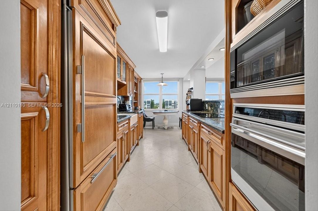 Kitchen featuring natural wood cabinetry, built-in panel-ready refrigerator, stainless steel double wall oven and microwave, dark stone countertops, and tile flooring