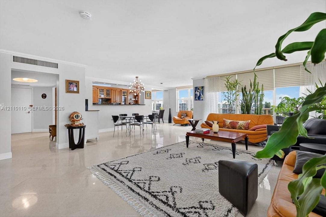 Open-concept interior featuring light-toned tile flooring, floor-to-ceiling windows, and a pass-through kitchen with built-in cabinetry and an attached breakfast bar