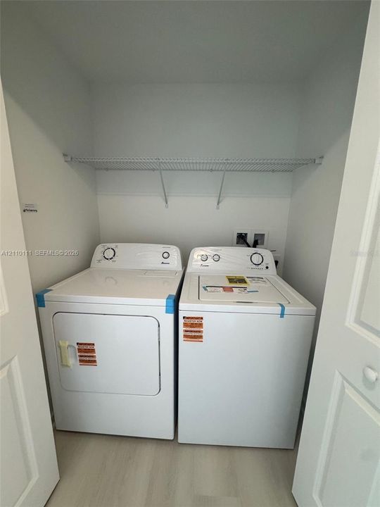 Laundry closet featuring side-by-side white washer and dryer units, a white wire shelf, and light-toned flooring