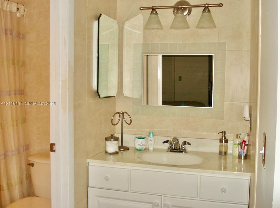Bathroom featuring a white vanity cabinet with an integrated sink, tri-light fixture, wall-mounted medicine cabinet with a glass-tile surround, and neutral-toned wall tiling