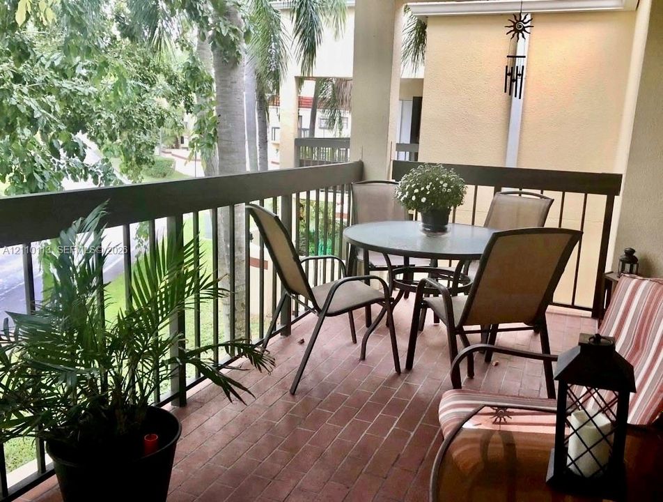 Covered balcony featuring red brick-style flooring and a dark metal railing