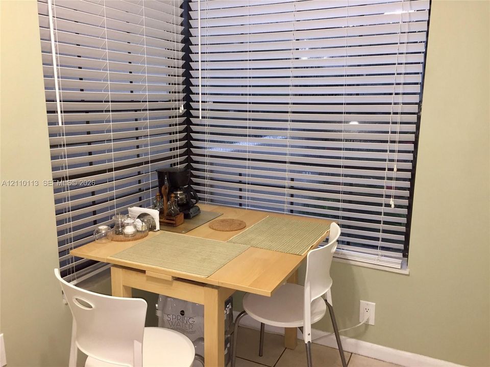 Corner window configuration featuring horizontal slat blinds and tile flooring