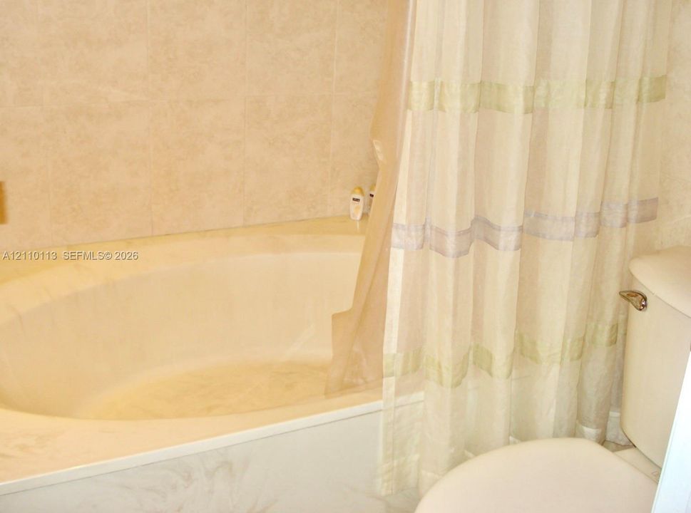 Oval soaking tub with a porcelain finish, accompanied by neutral-toned wall tile surround and a standard toilet